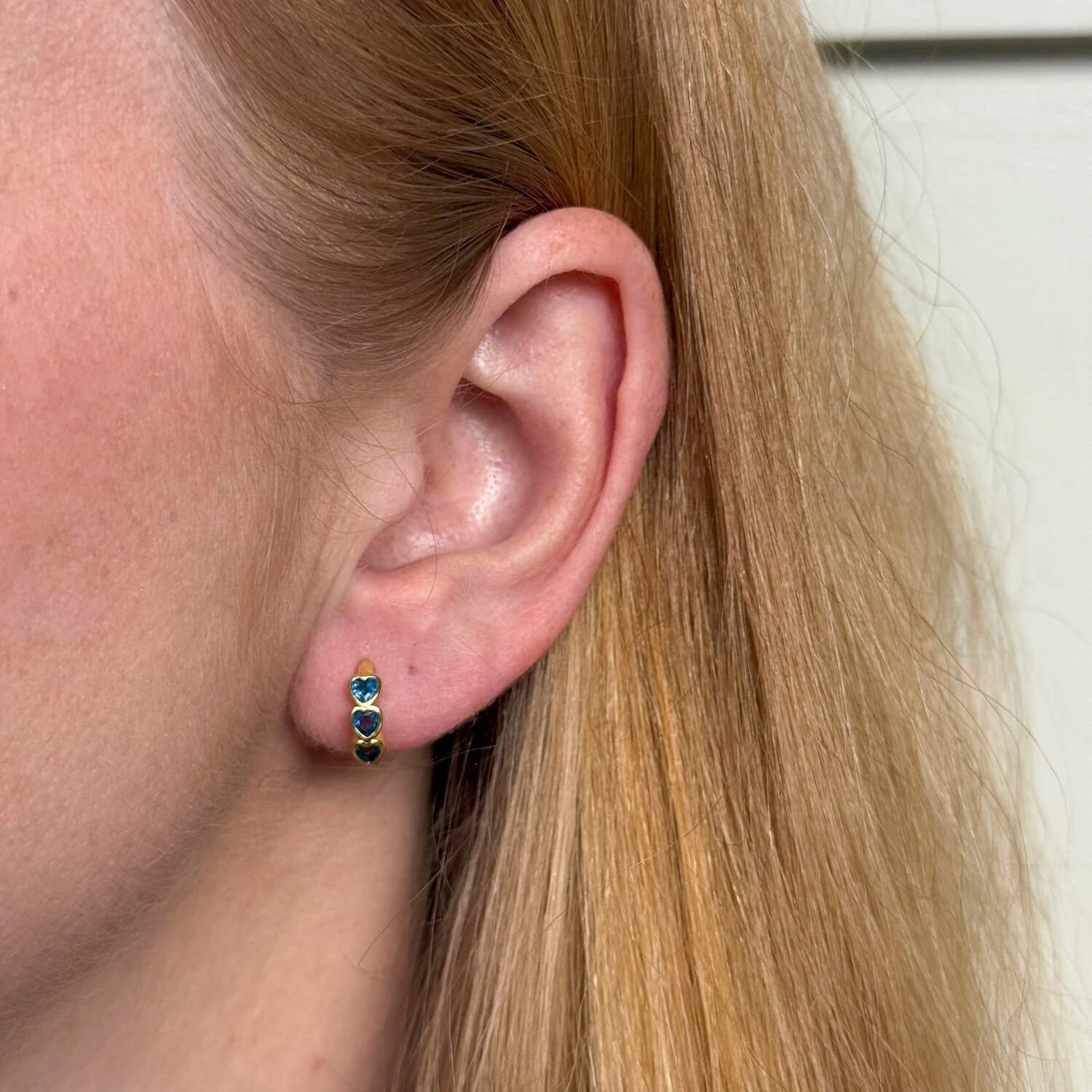 Model wearing gold plated huggie earrings with bezel-set blue heart, minimalist everyday jewellery. - Solinu Jewellery