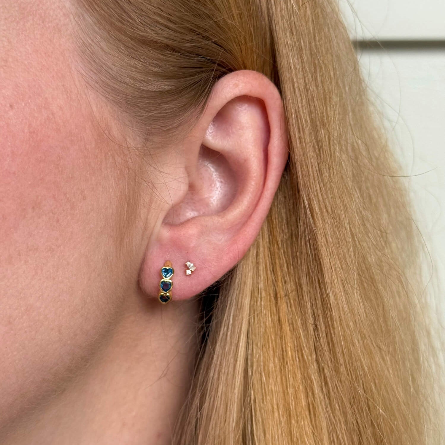 Model wearing gold plated huggie earings with bezel-set blue heart, casual everyday jewellery. - Solinu Jewellery