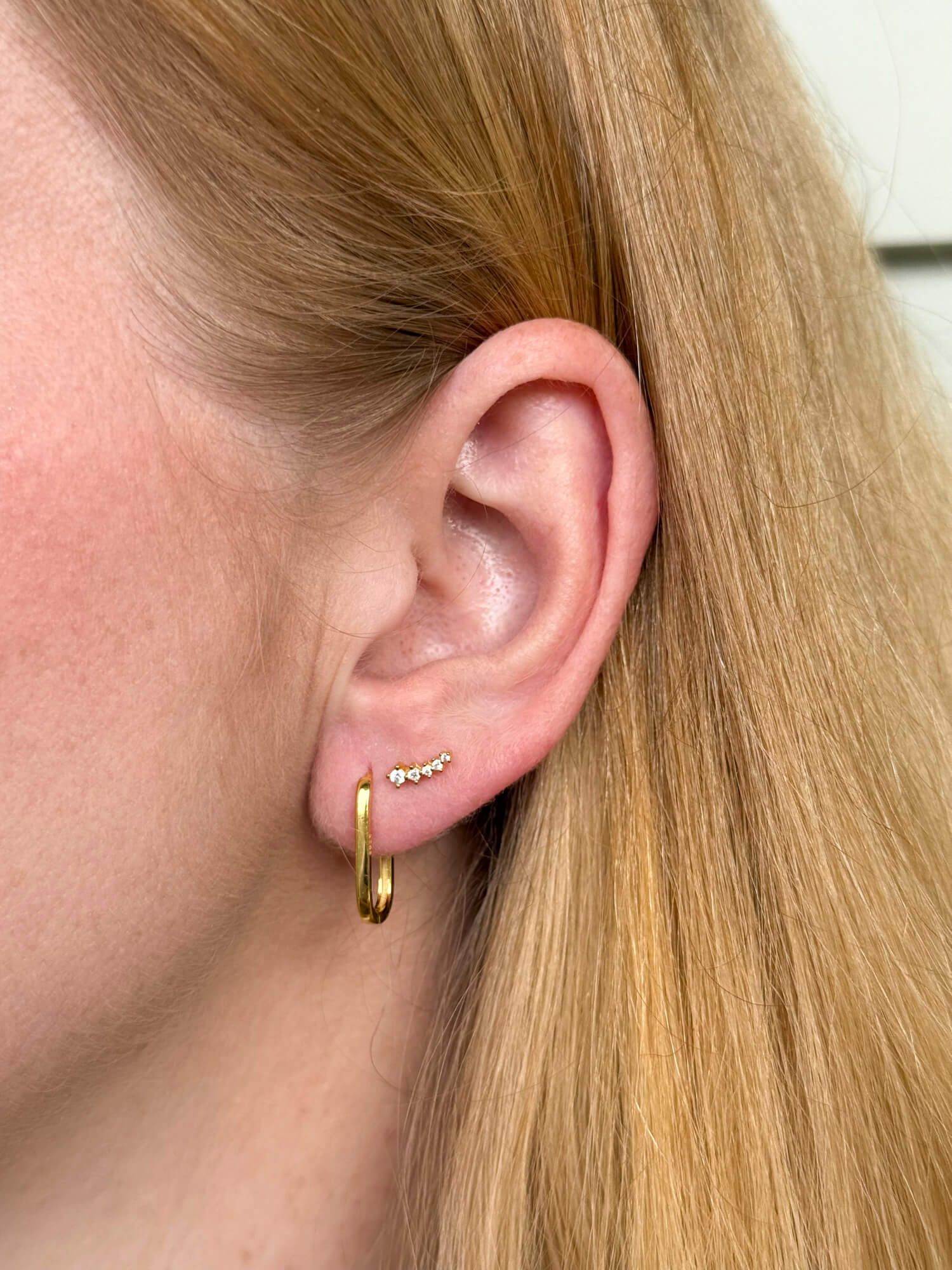 Model wearing gold-plated on sterling silver elongated hoop earrings with sleek minimalist silhouette, paired with sparkle ear crawler. - Solinu Jewellery 