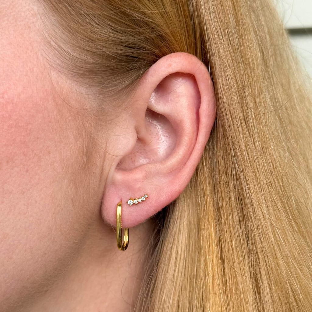 Model wearing gold-plated on sterling silver elongated hoop earrings with sleek minimalist silhouette, paired with sparkle ear crawler. - Solinu Jewellery 