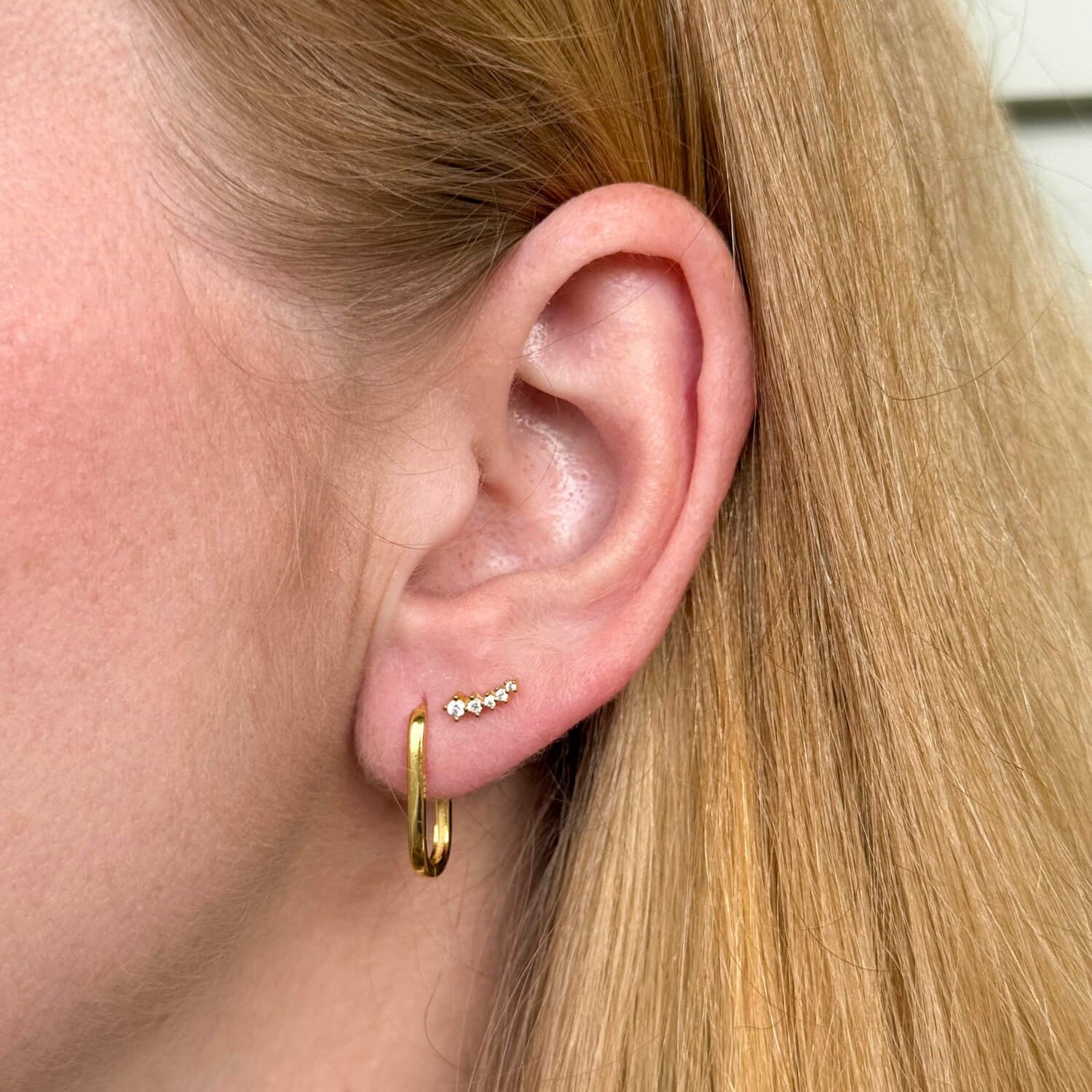 Model wearing gold-plated on sterling silver elongated hoop earrings with sleek minimalist silhouette, paired with sparkle ear crawler. - Solinu Jewellery 